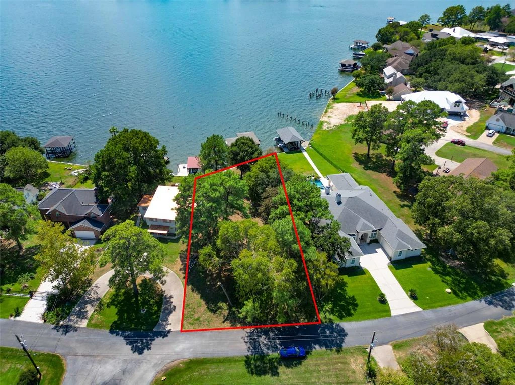 Angled aerial view of a waterfront lot outlined in red, with the shoreline, neighboring homes, and open water visible.